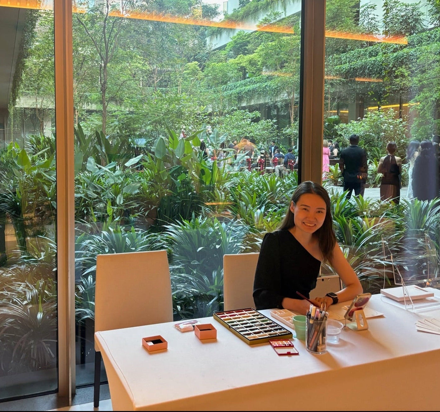 Woman sitting at a table with a view of a garden through large windows.
