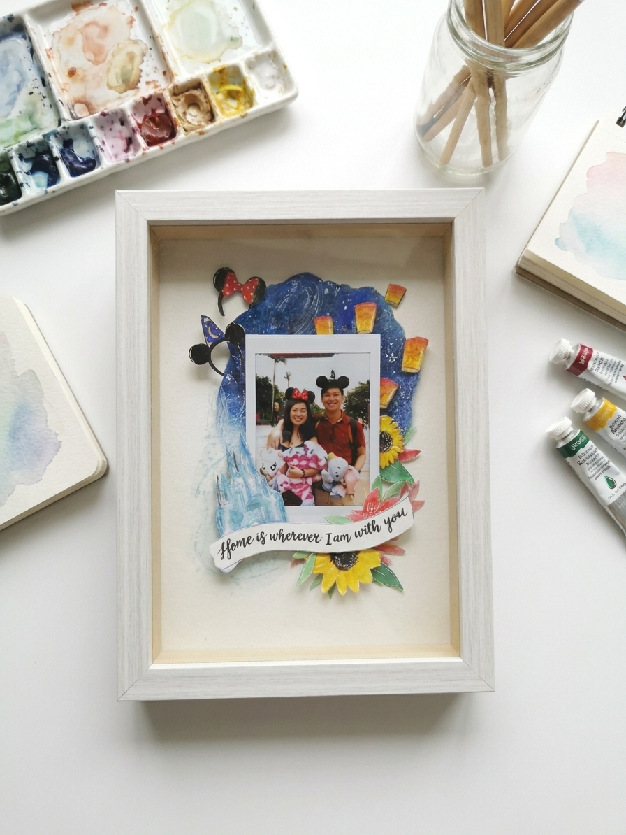 Decorative shadow box with a photo of two people and colorful decorations on a white surface.