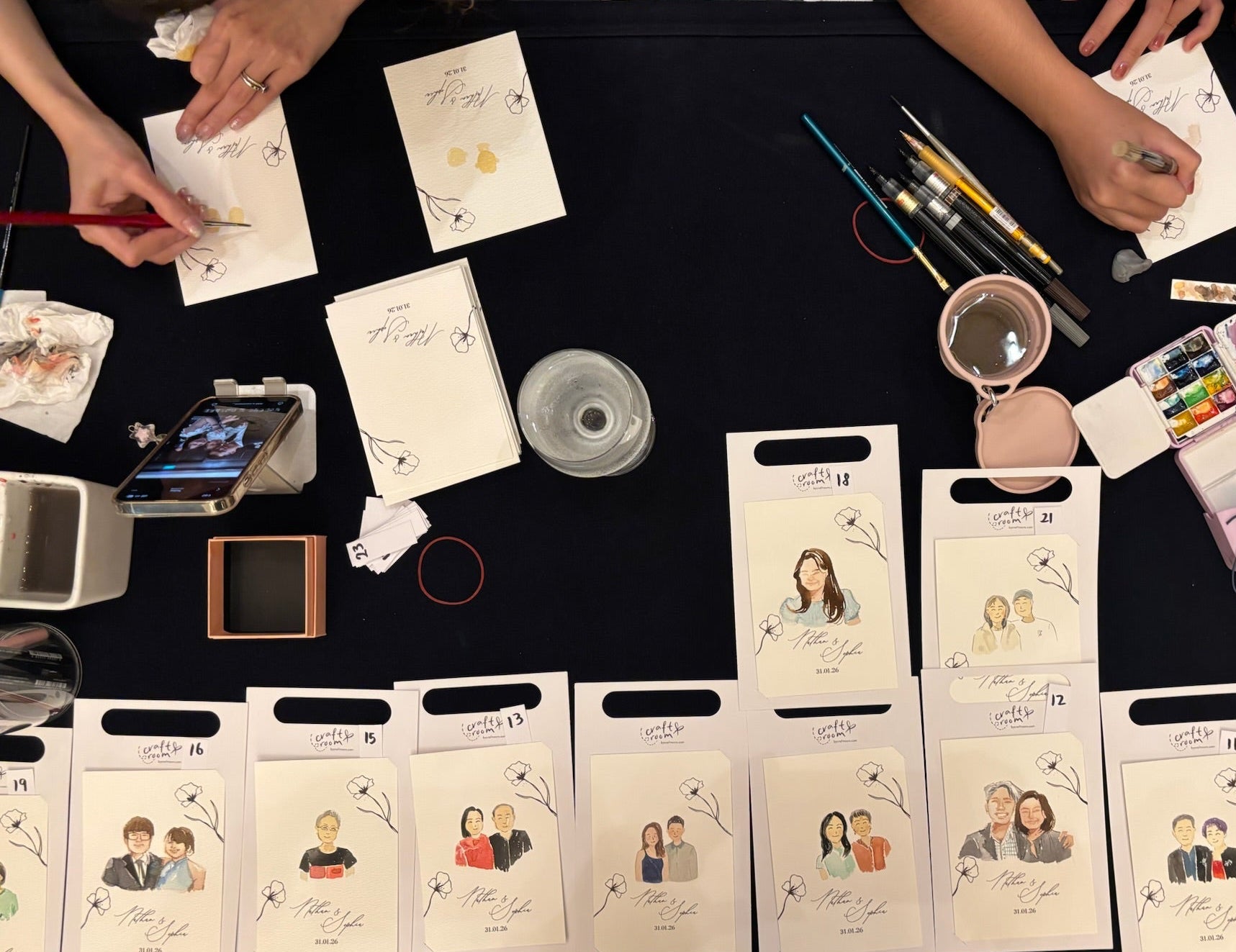 Table with printed cards and stationery items, with people working on a project.
