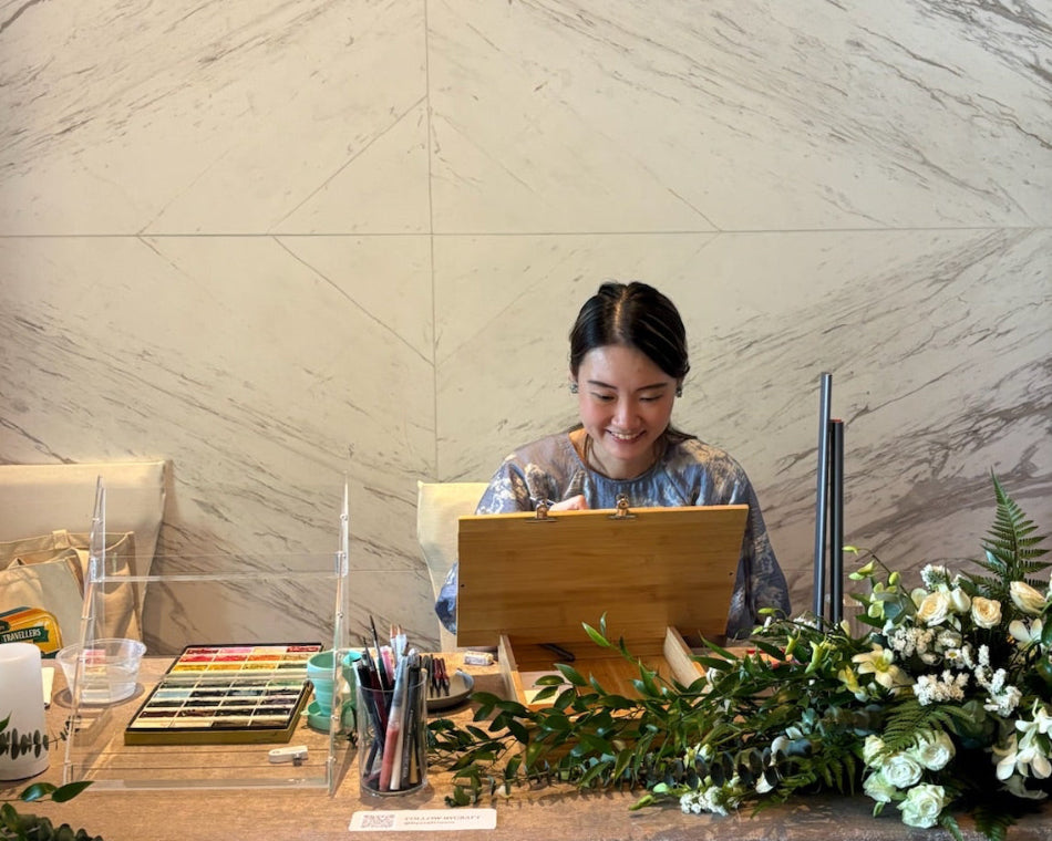 Person sitting at a desk with a laptop, surrounded by flowers and stationery, against a marble wall.