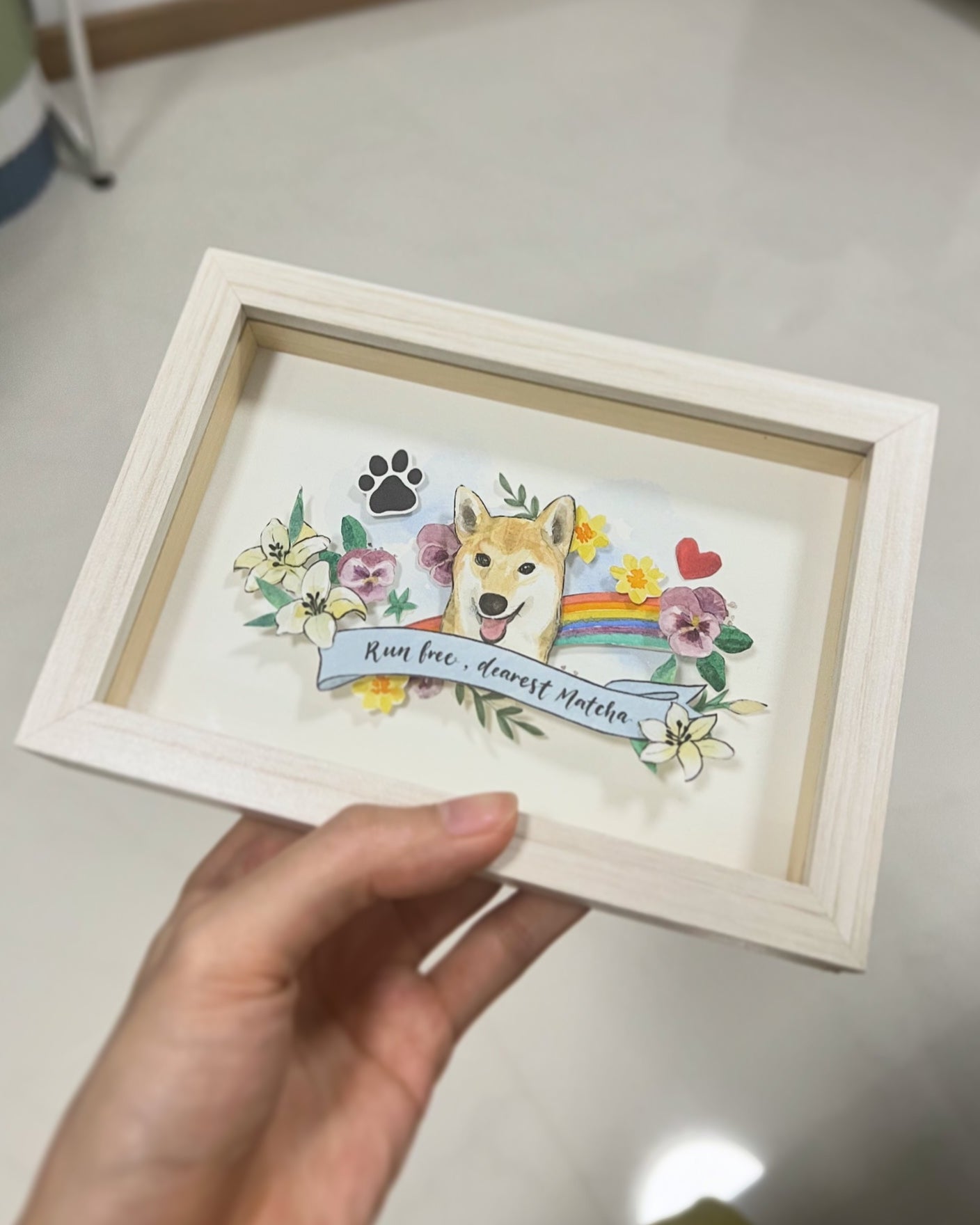 Framed artwork of a dog with floral elements and text held by a hand.