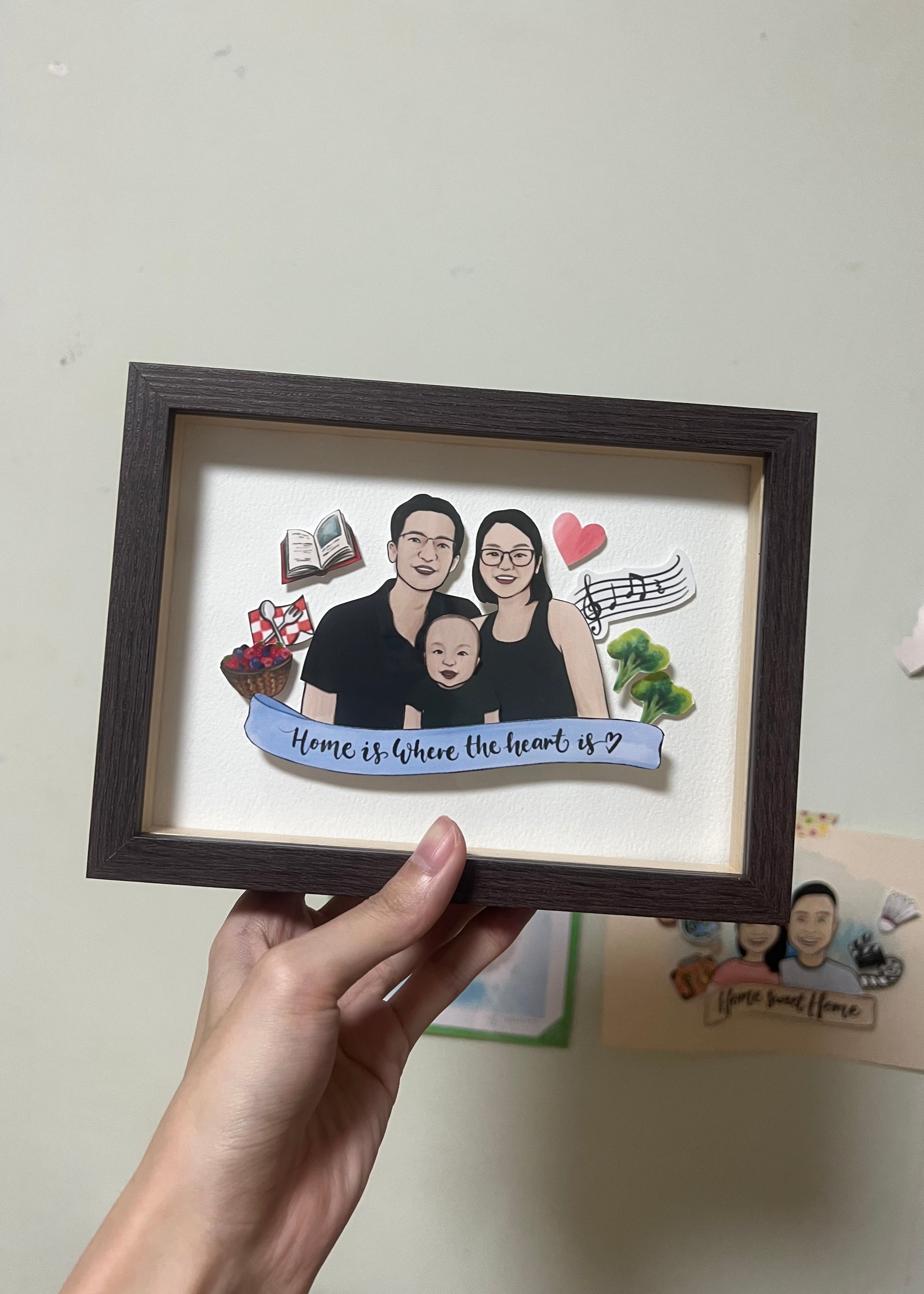 Framed artwork with a family portrait and text held by a hand against a light background