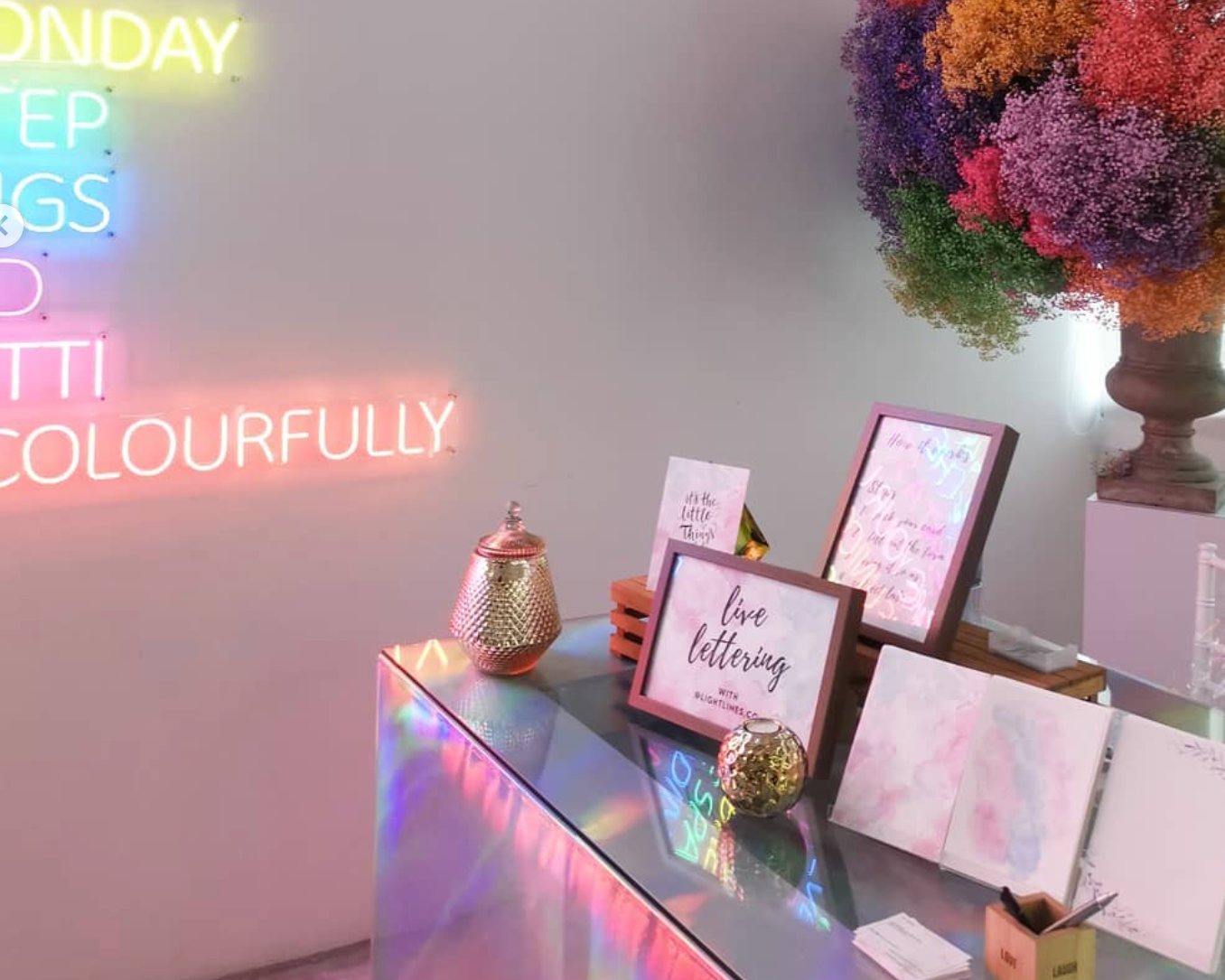 Neon sign with colorful letters on a wall above a desk with decorative items.