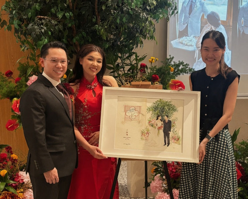 Three people holding a framed picture in a decorated indoor setting with flowers and a screen in the background.