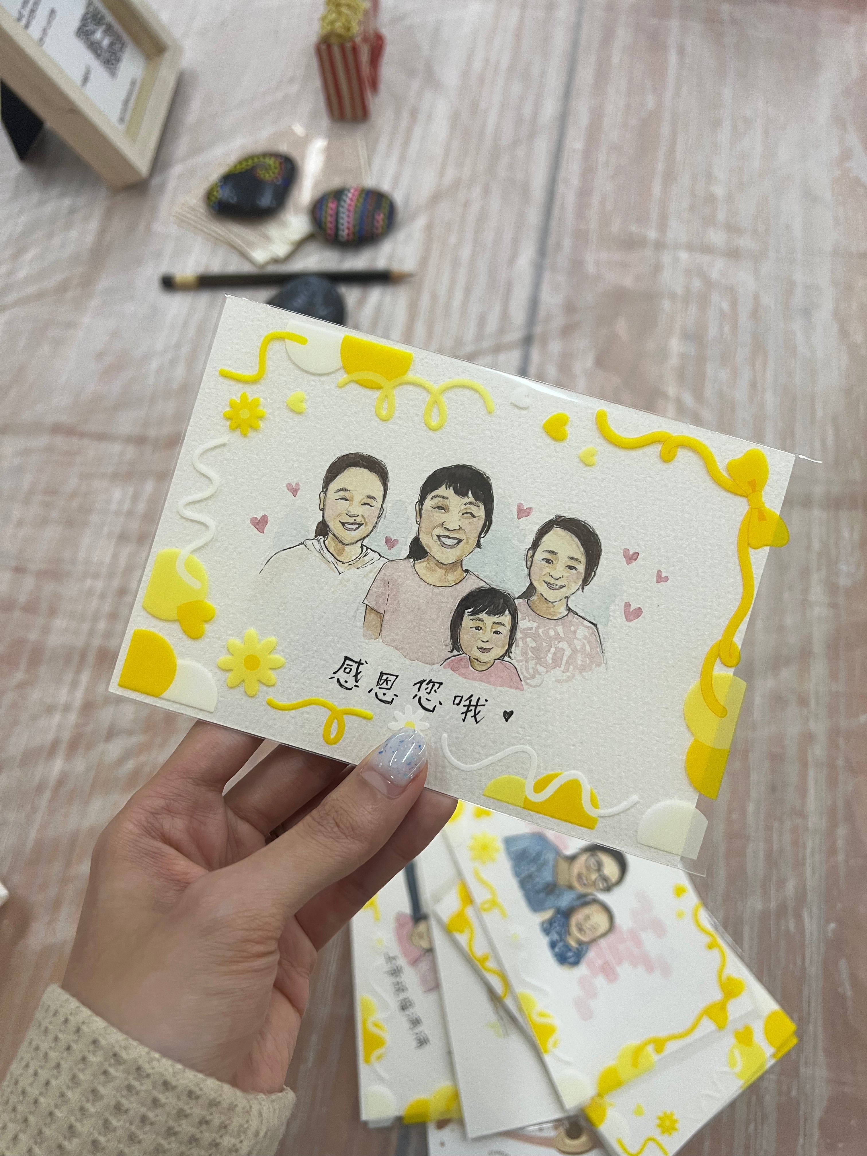 Hand holding a card with a family illustration and decorative elements on a wooden surface.