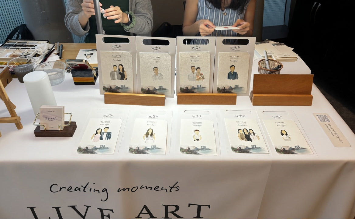 Two women at a table with photo albums and a banner reading 'LIVE ART'.