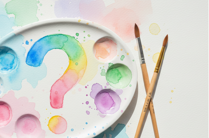 Colorful paint palette with a question mark and two brushes on a watercolor splatter background