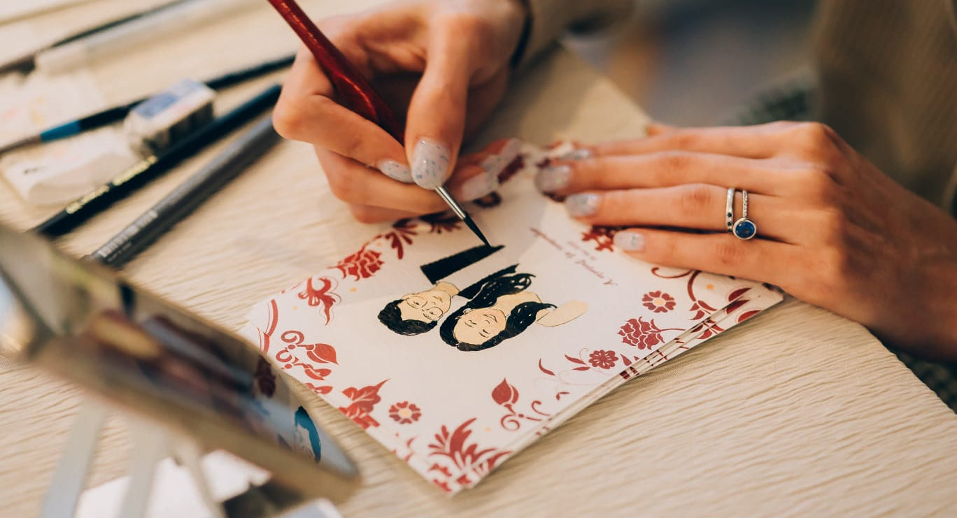 Person painting a design on a small watercolor paper with brushes and paint.