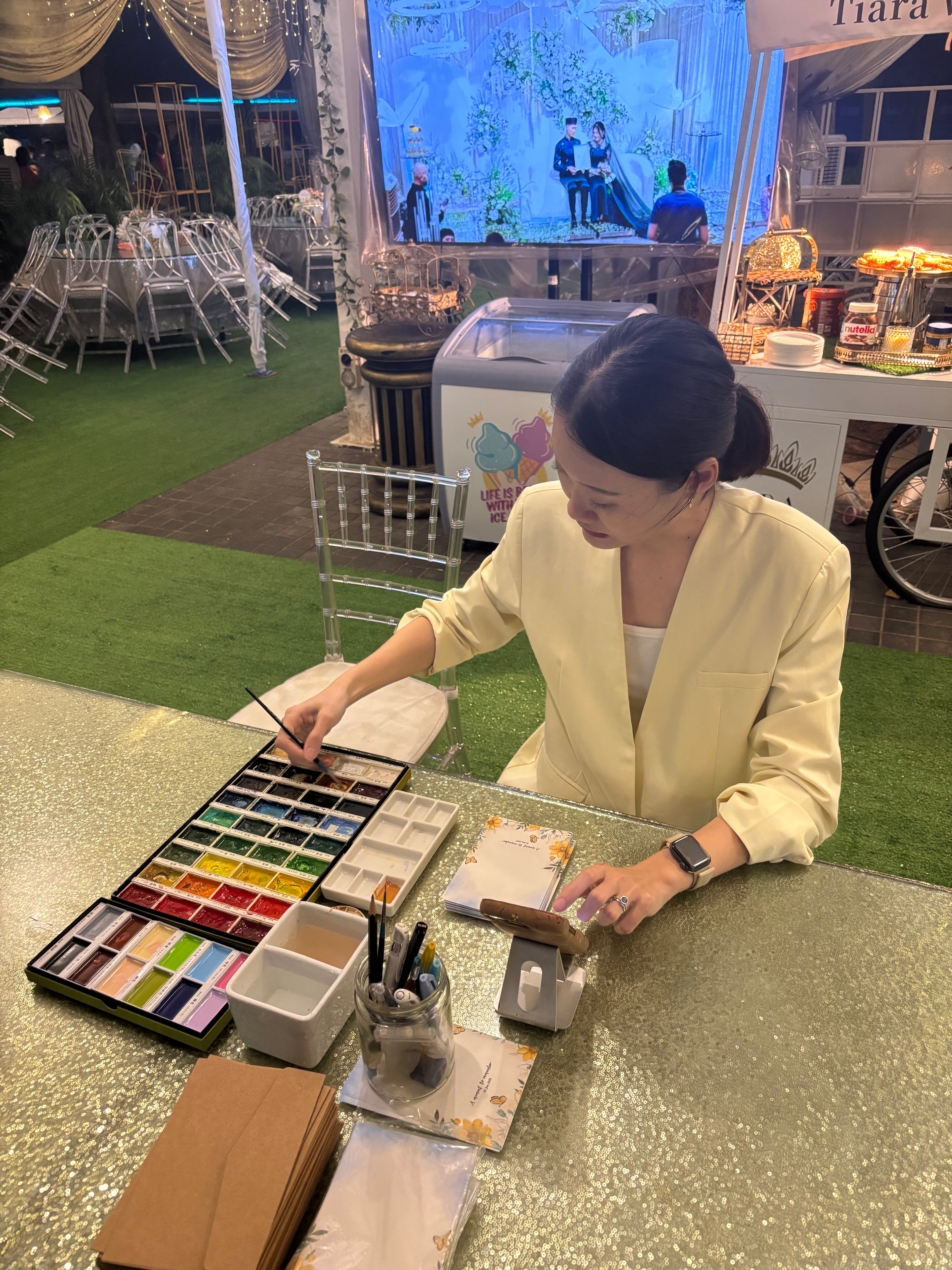 Woman working with art supplies at a table in an outdoor event setting