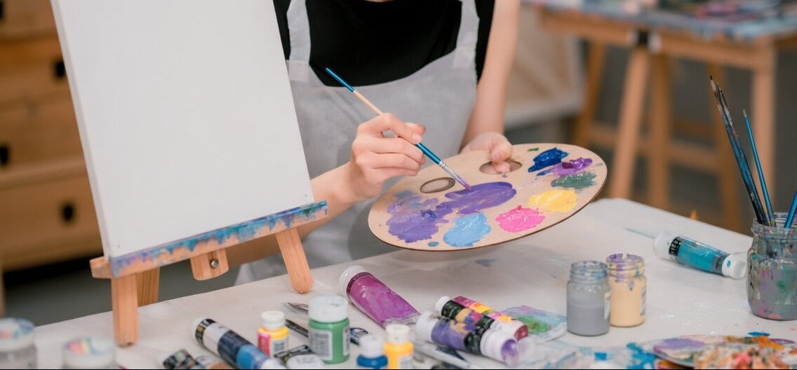 Artist painting on a canvas with various art supplies around