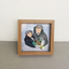 A couple in winter outfit drawing holding a mini dried flower bouquet in a wood frame.