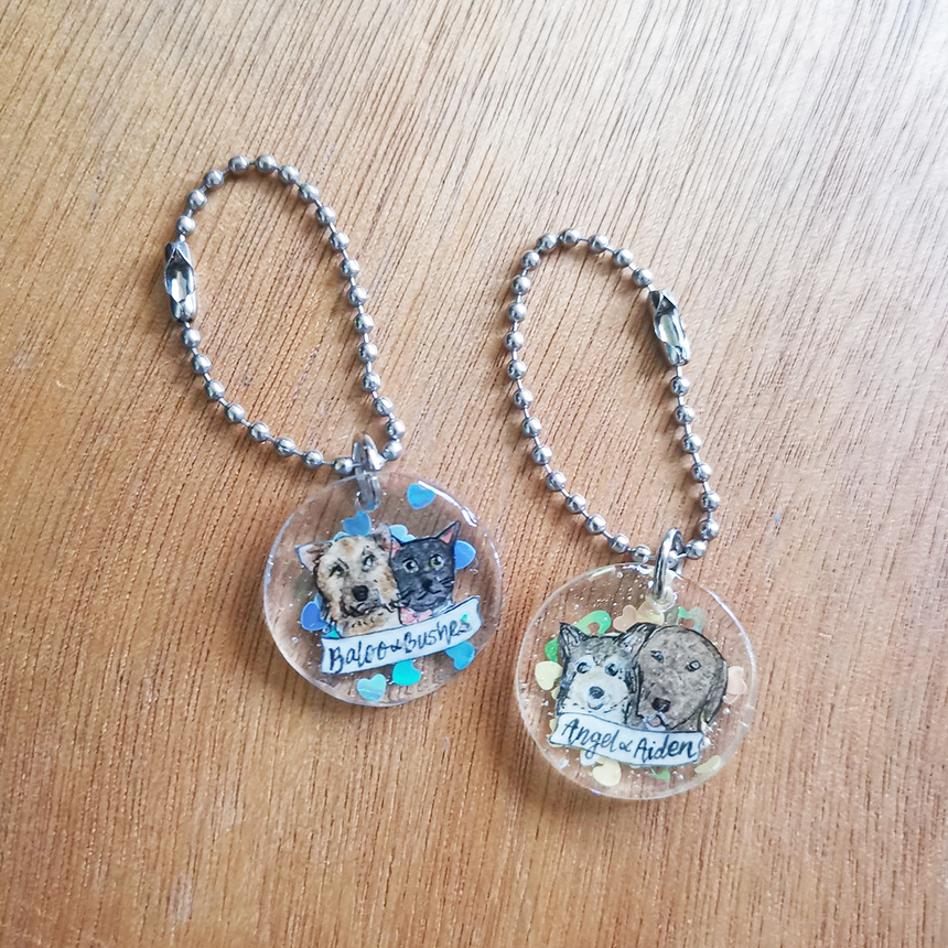 Two pet with personalised name banners keychains in round shaped.