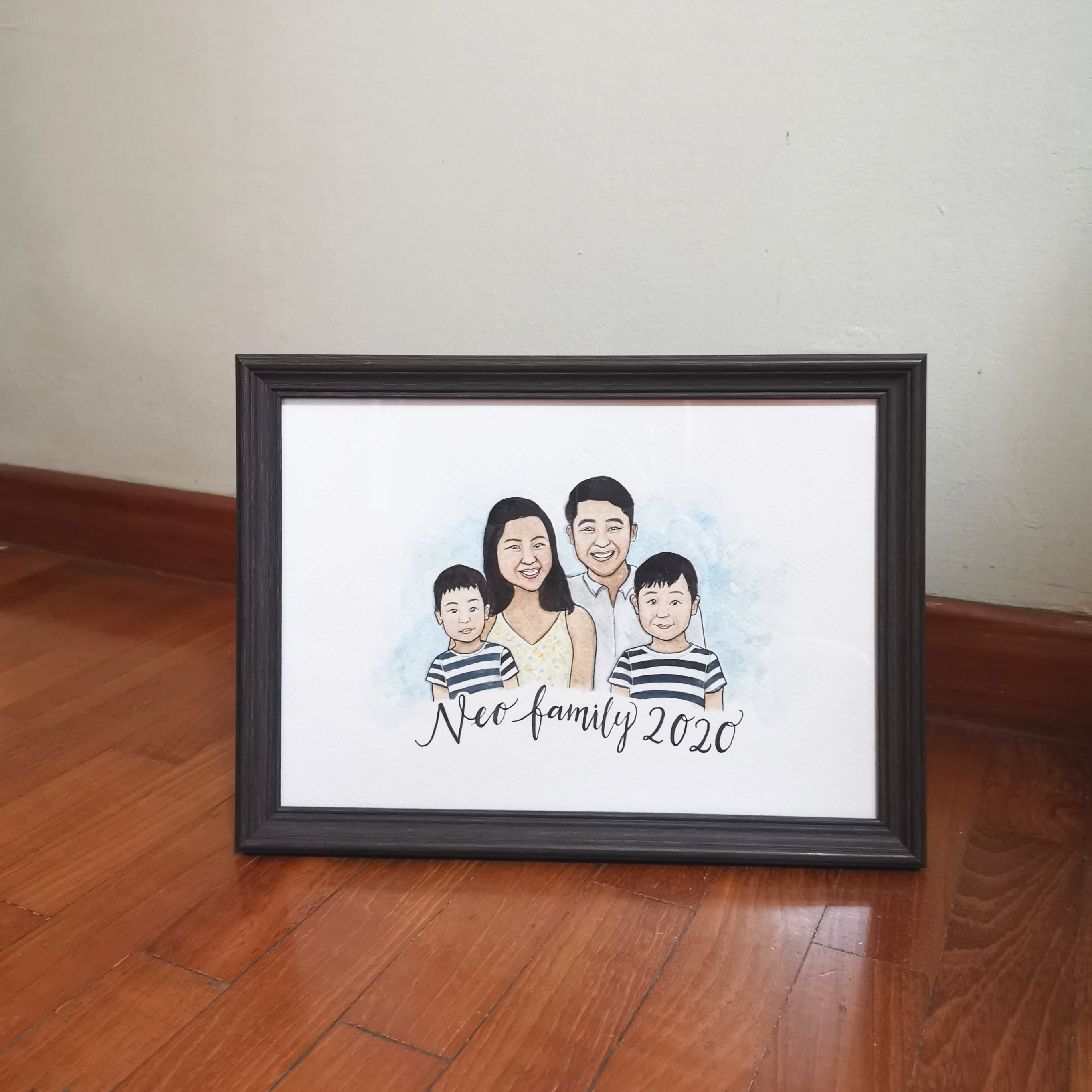 A watercolor family portrait of four members in a black A3 frame.